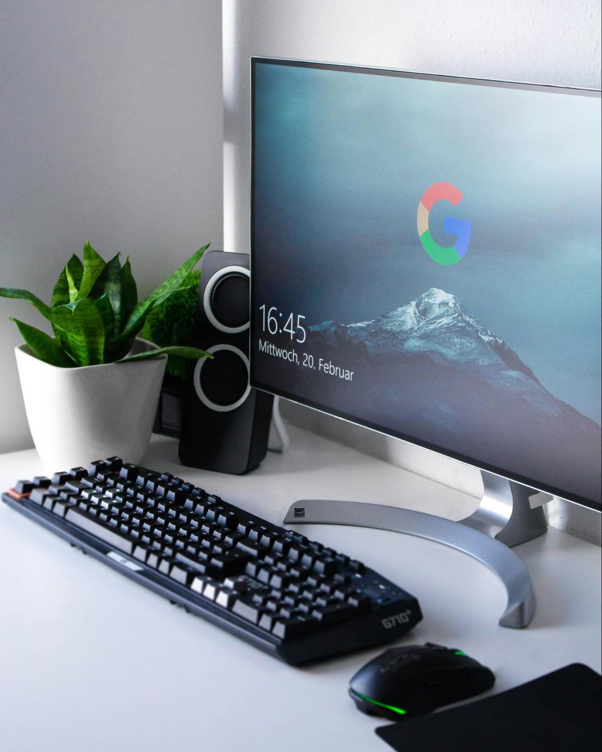 Curved monitor showing a Google logo wallpaper next to a keyboard and a plant