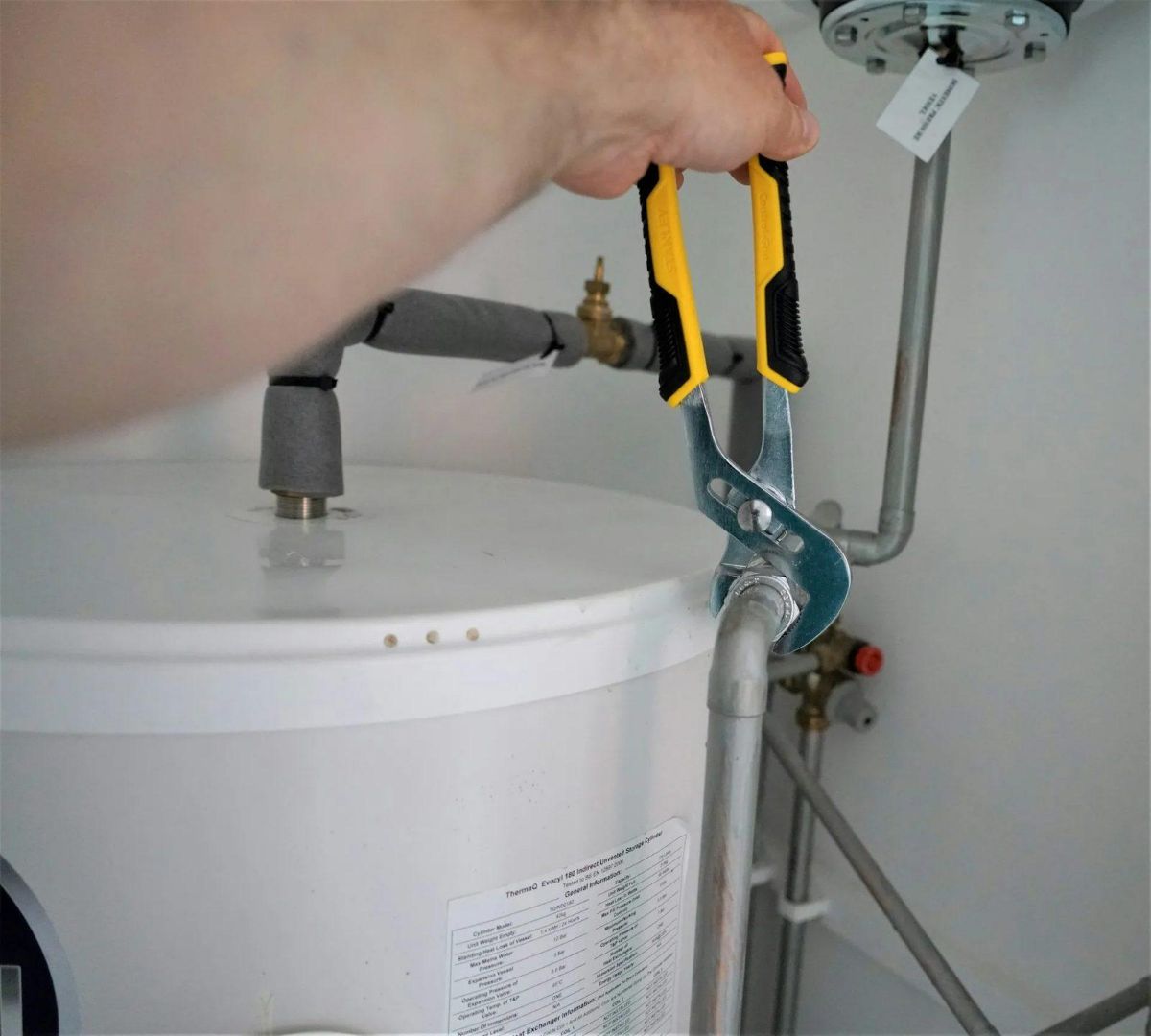 Hand using adjustable pliers on a pipe fitting at a water heater tank