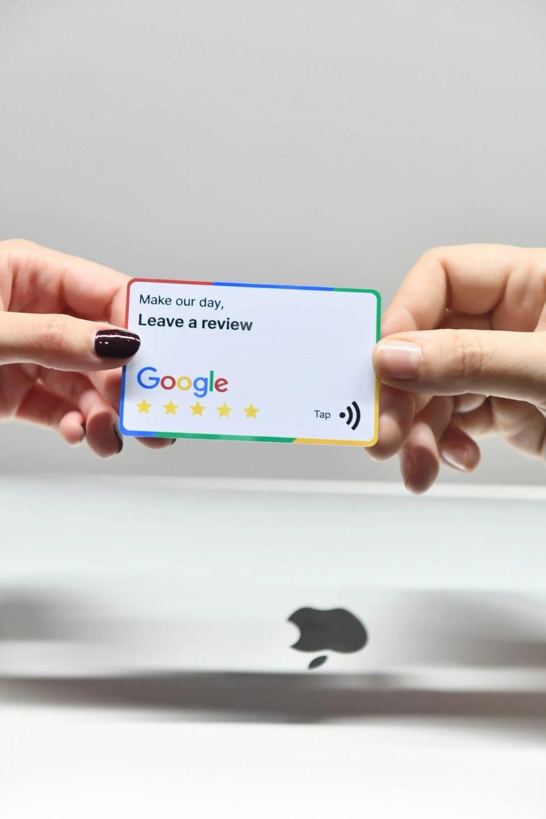 Two hands holding a tap-to-review card with the Google logo and five stars