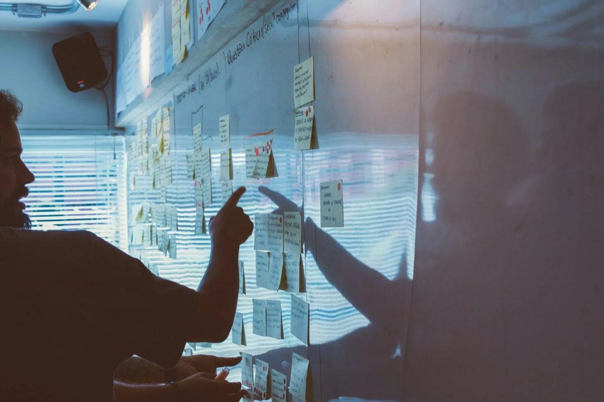 Person pointing at sticky notes on a glass wall during a planning session