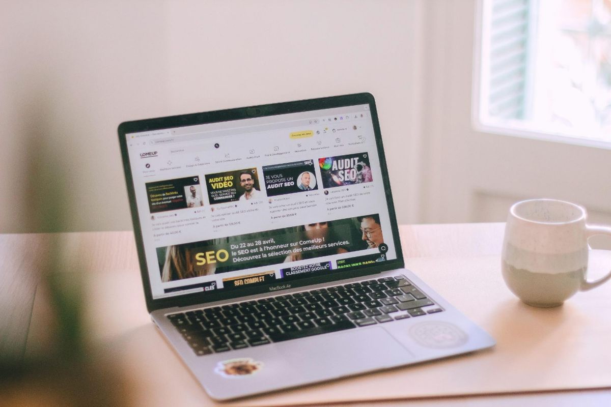 Laptop on a wooden table showing a freelance services website beside a mug