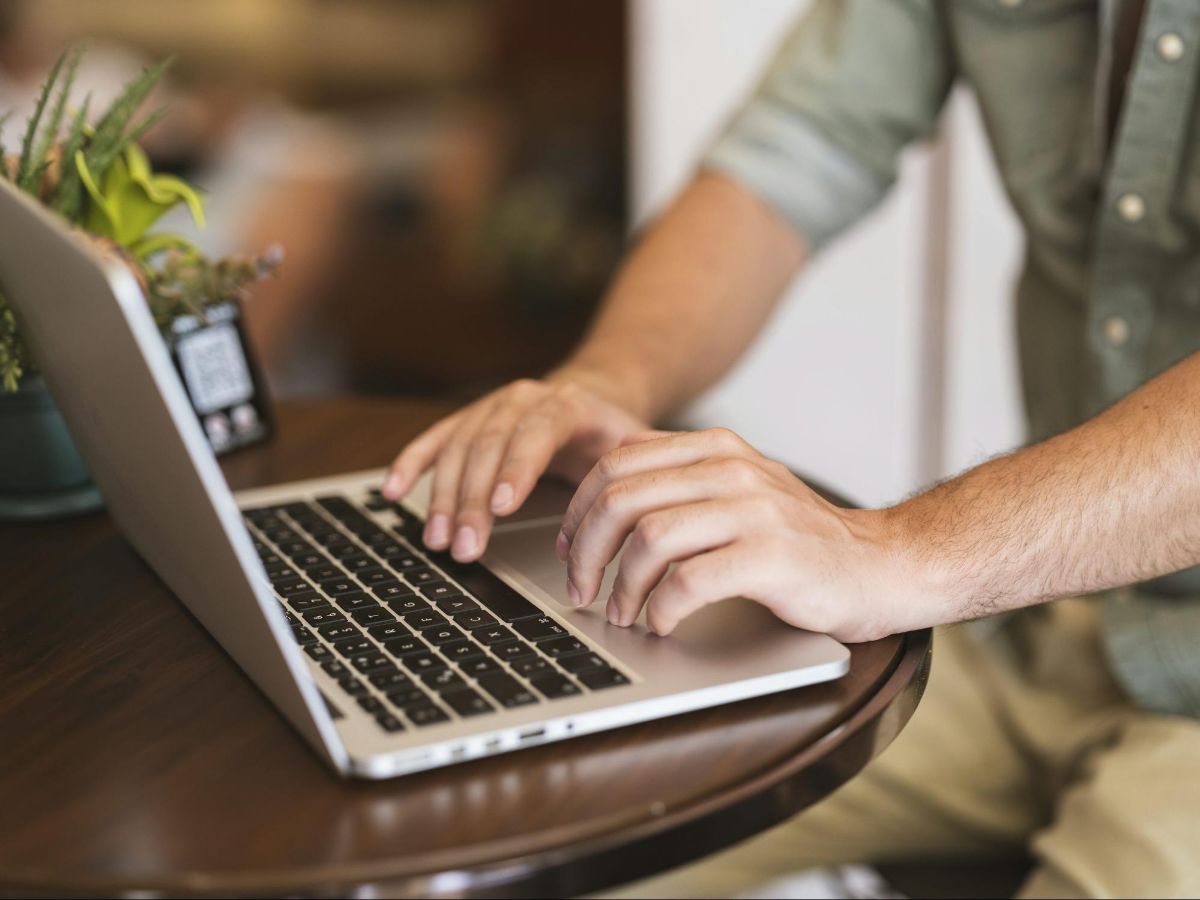 Hands typing on a silver laptop on a round wooden table