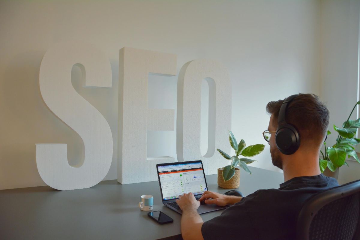 Man in headphones working on a laptop beside large white letters spelling SEO