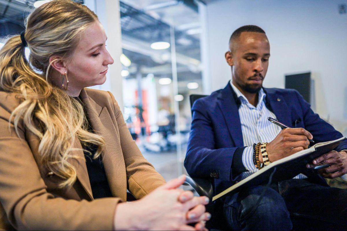 Woman in a tan blazer listening while a man takes notes