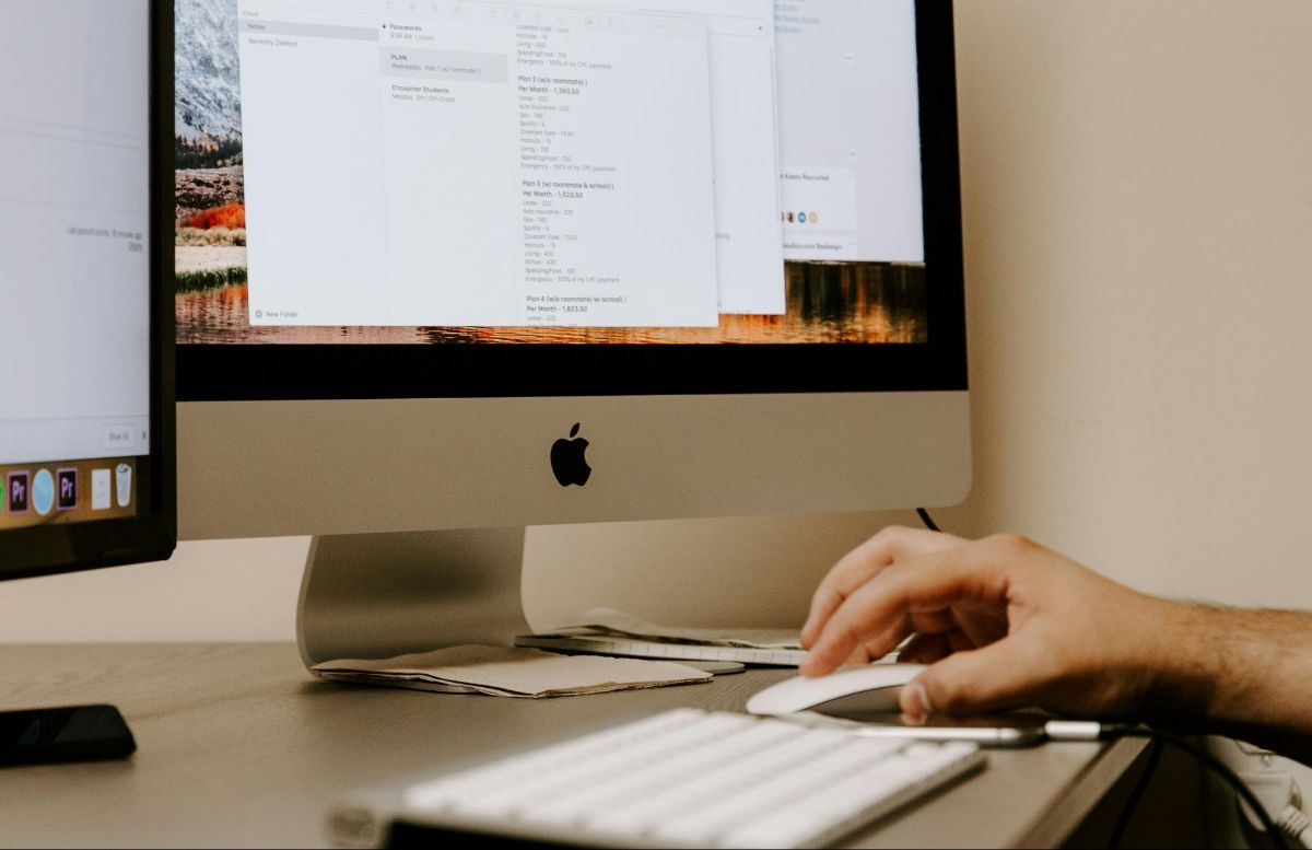 Hand on a computer mouse in front of a desktop monitor with open documents