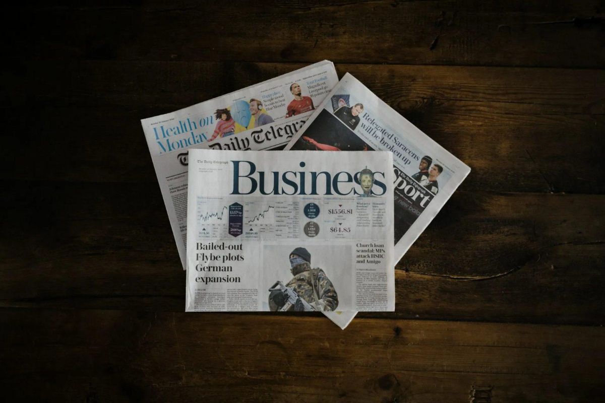 Newspapers fanned out on a dark wooden table