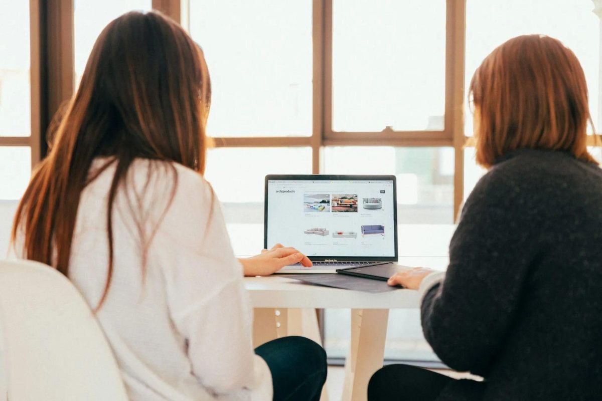 Two women at a desk looking at a website on a laptop