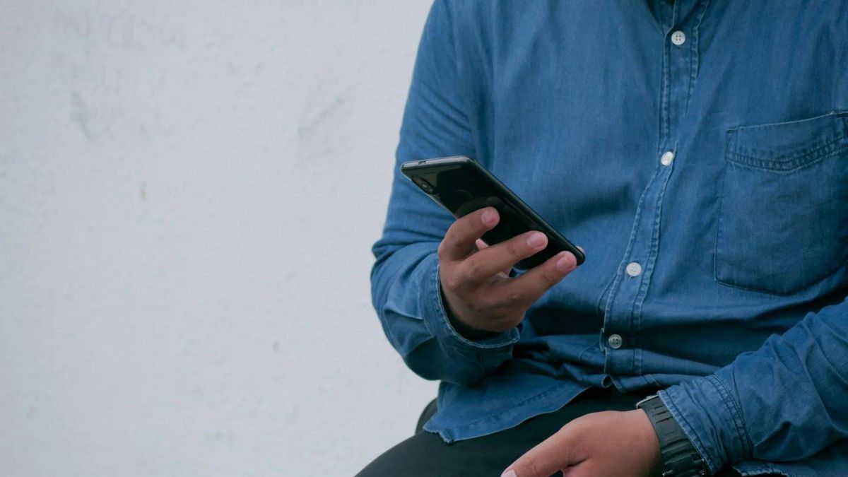 Person in a denim shirt holding a black smartphone