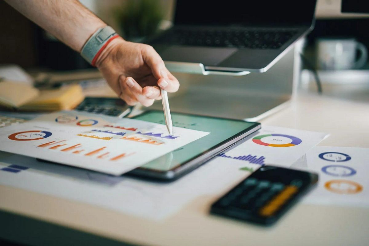 Person pointing a stylus at a tablet surrounded by printed charts