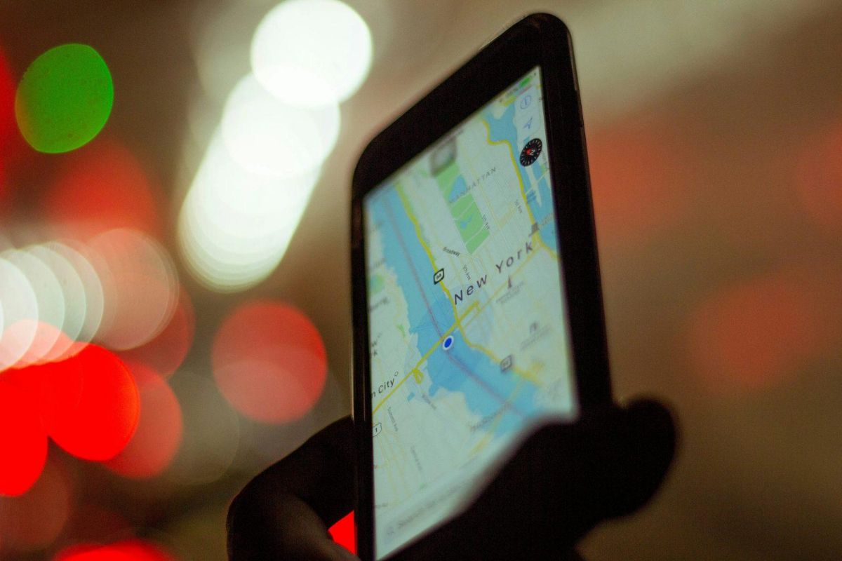 Hand holding a phone with a map of New York against blurred city lights