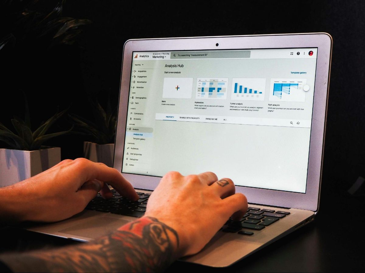 Tattooed hands typing on a laptop showing Google Analytics reports