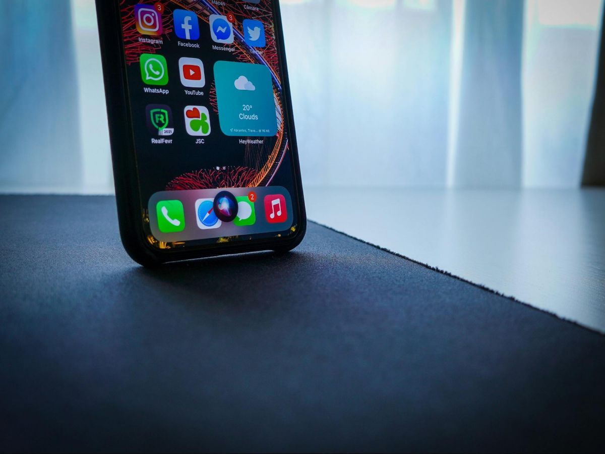 Phone standing on a desk with apps on the screen and Siri listening